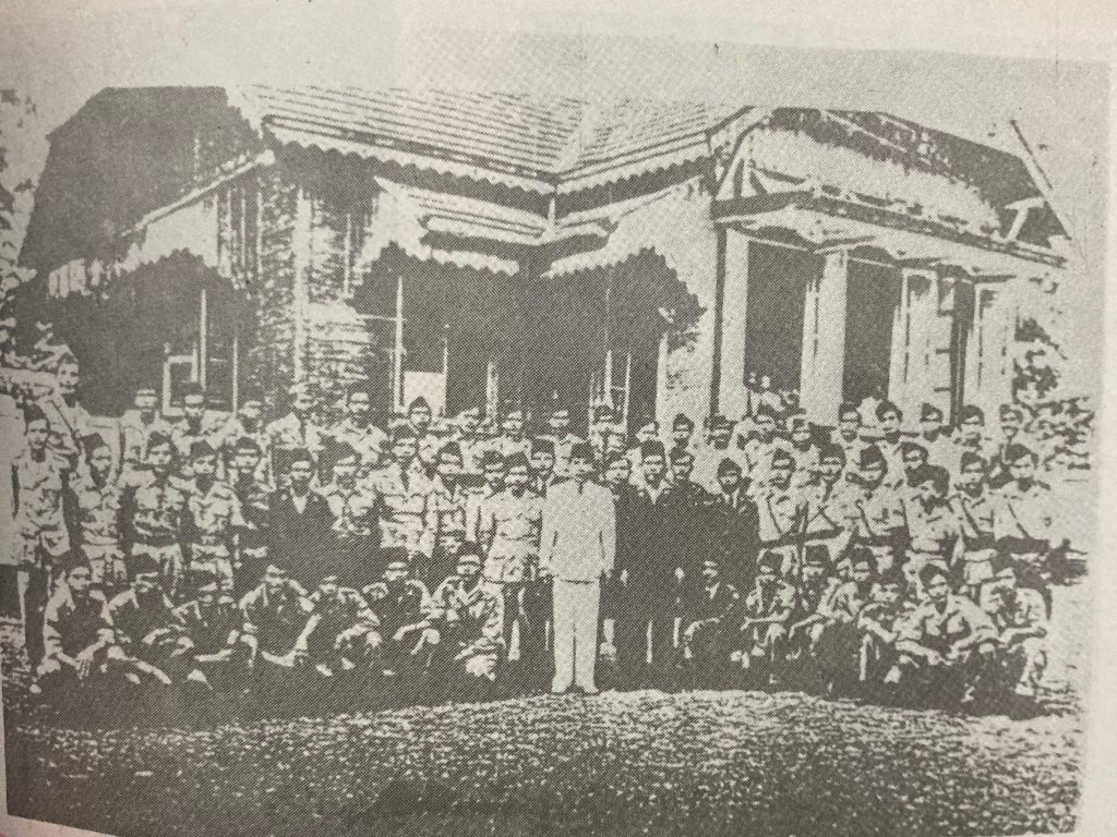 Historic photograph featuring a group of soldiers and civilians standing in front of a building, capturing a moment from Indonesian history.